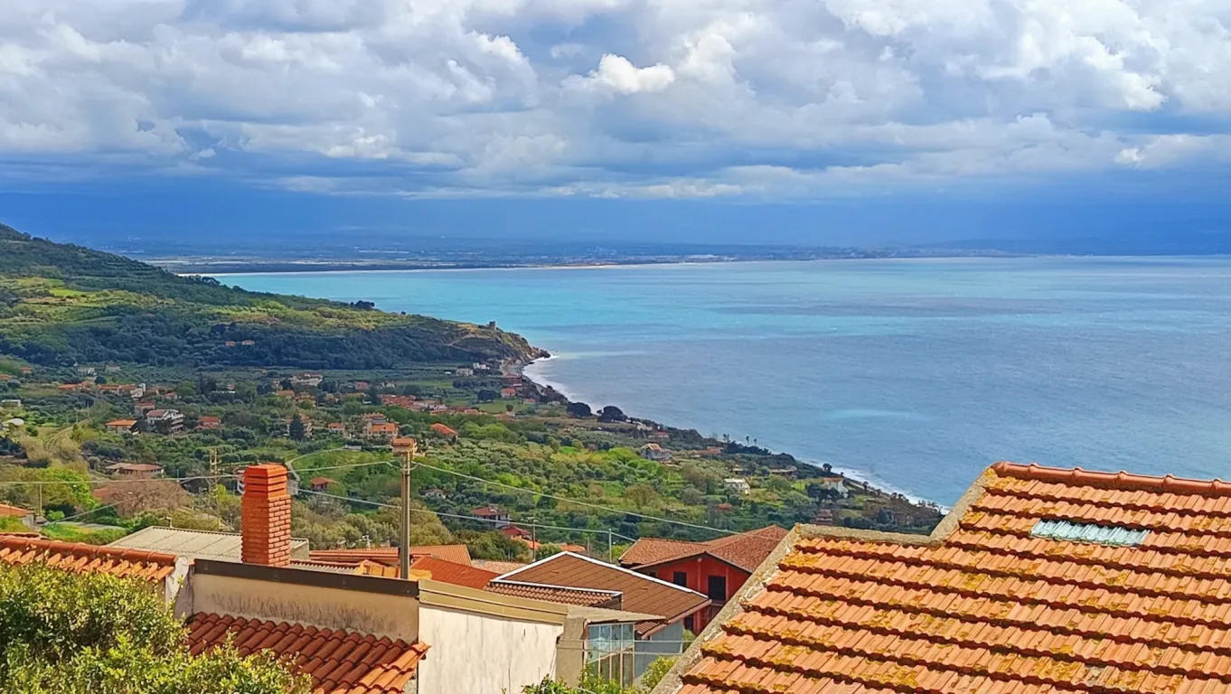 Blick über Ziegeldächer auf den Golf von Gioia Tauro, die grüne Küste und einen langen hellen Sandstrand.