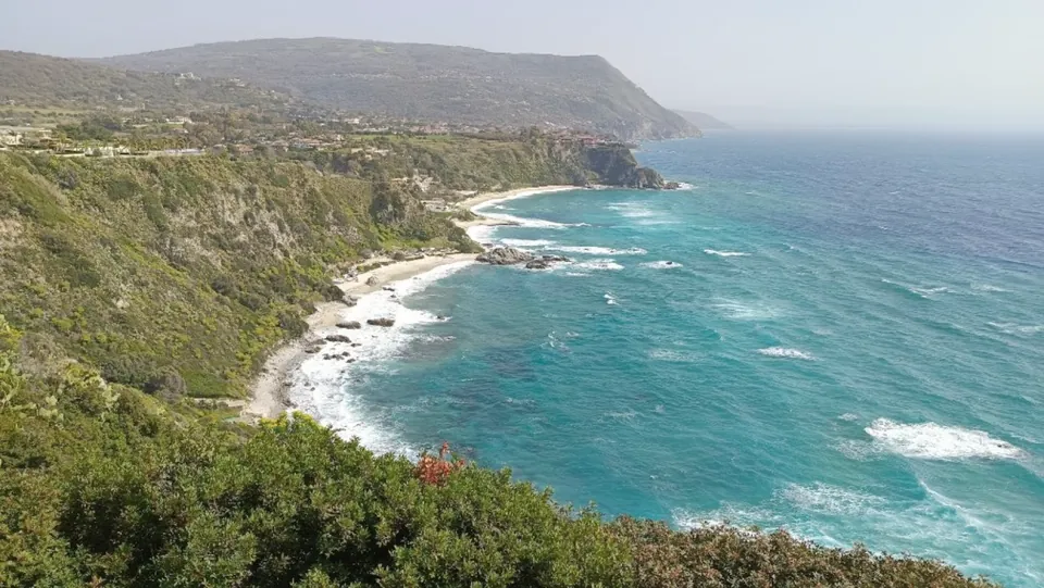 Steilküste mit grünen Hängen, türkisfarbenem Wasser und kleinen Buchten.