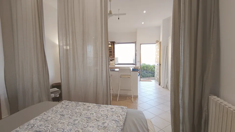 Blick vom Bett durch die offene Tür zur Küche und zum hellen Fenster.