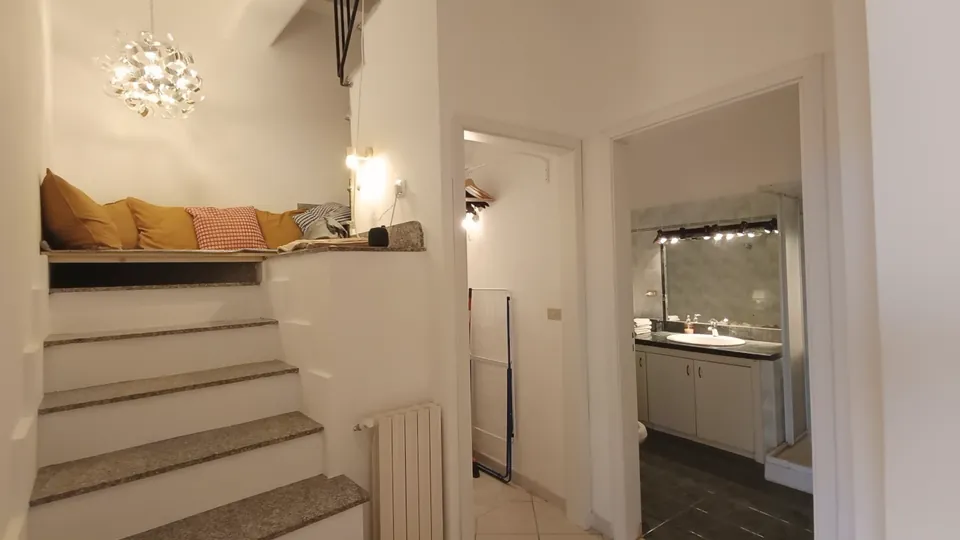 Eine stillgelegte Treppe mit Kissen als Sitzecke, dahinter ein Abstellraum und das Bad.