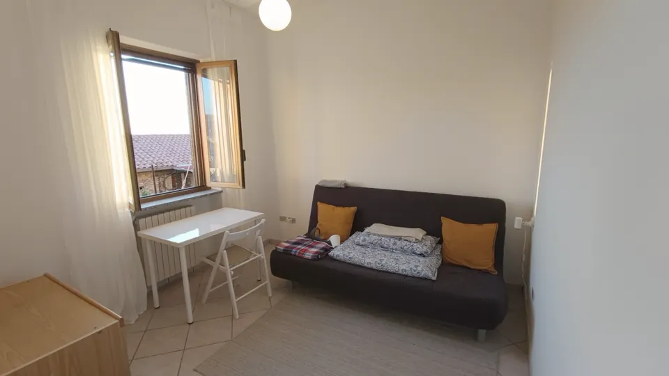 Das zweite Zimmer mit Schlafsofa, kleinem weißen Tisch und einem Fenster mit Blick auf Dächer.