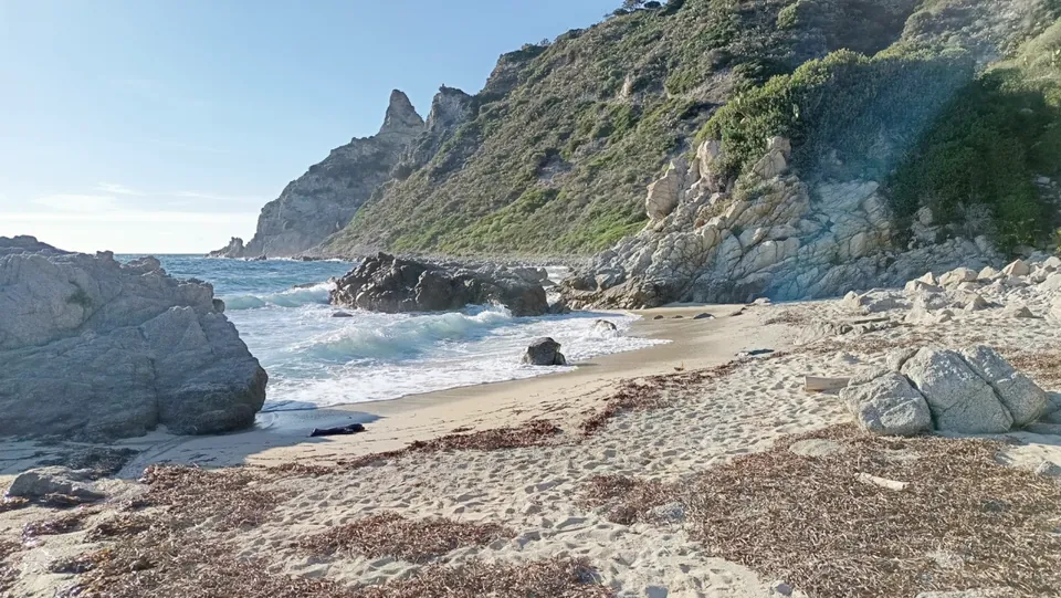 Kleine Bucht mit Sandstrand zwischen Felsen, dahinter eine Steilküste.